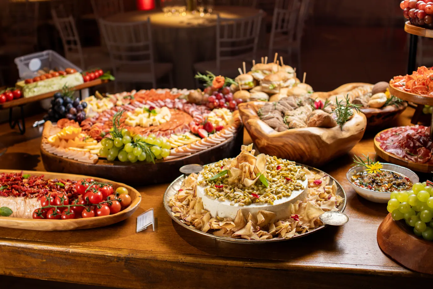 Mesa de buffet de formatura com pães, frutas, frios e antepastos.