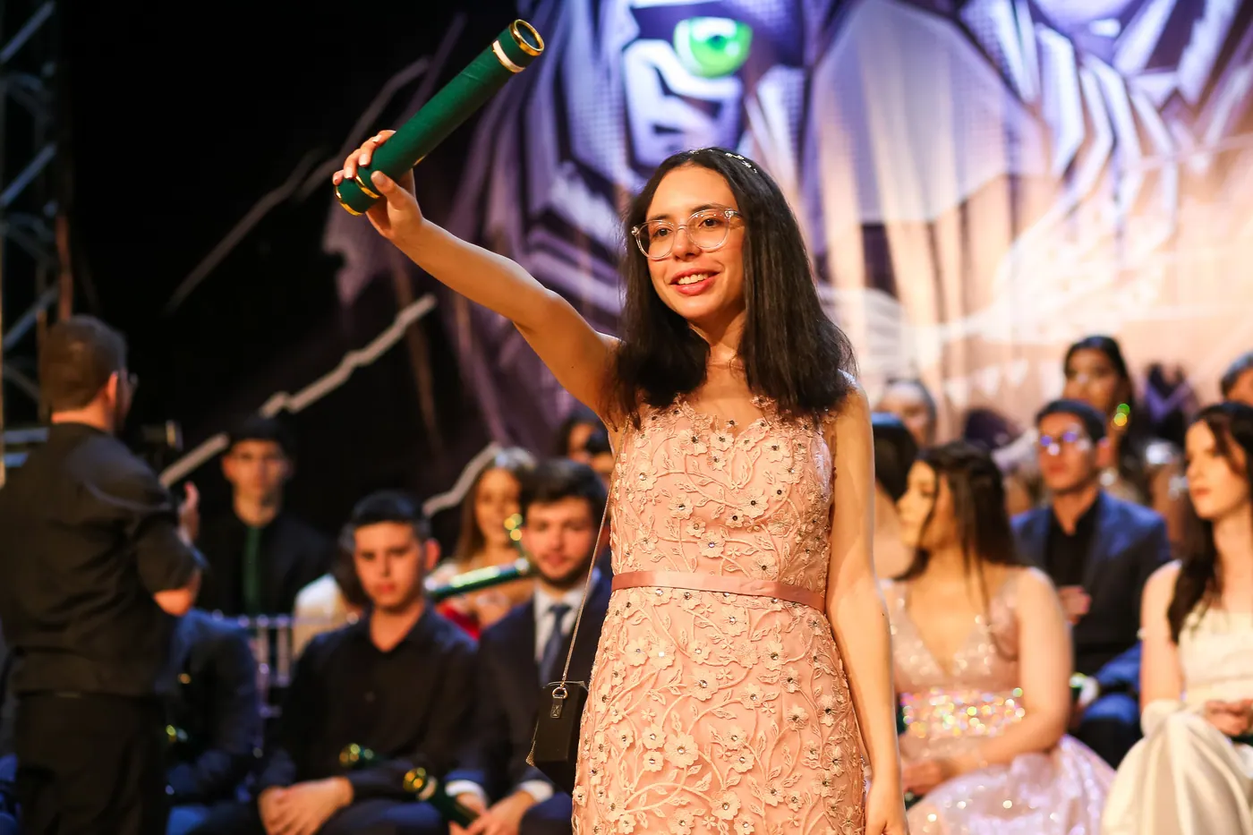 Formanda sorrindo e levantando o canudo durante a cerimônia.