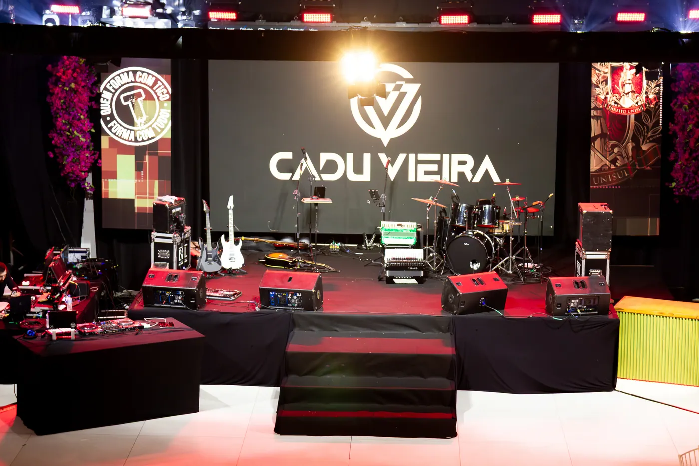 Palco de formatura preparado com painéis de LED, flores e iluminação vermelha.