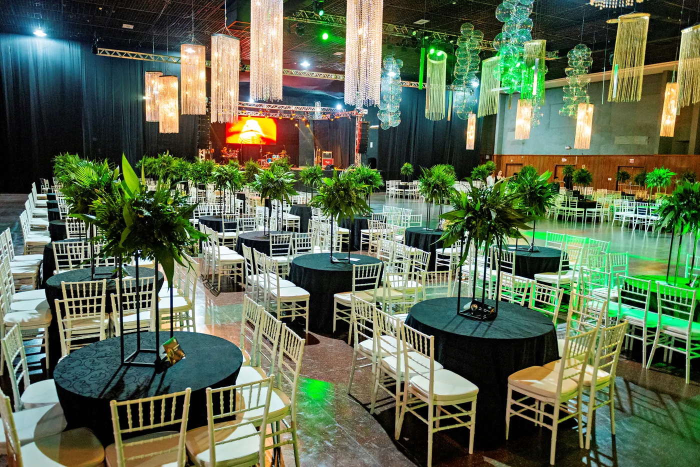 Salão de formatura com mesas, plantas e iluminação verde.