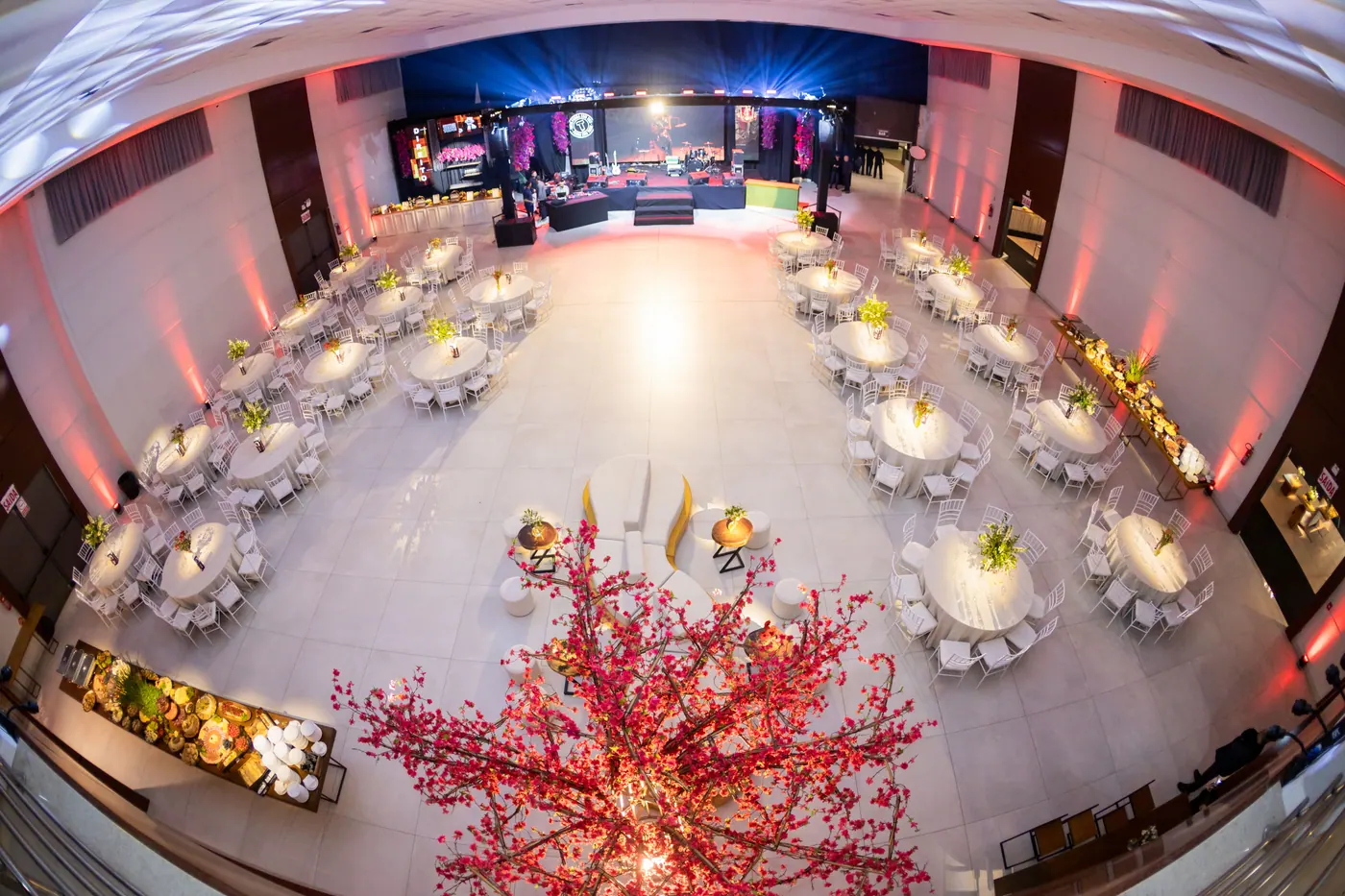 Vista ampla do salão de formatura com mesas preparadas e palco iluminado.