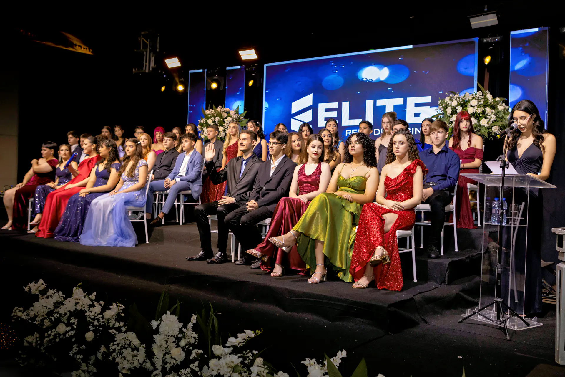Turma de formandos reunida no palco durante cerimônia de formatura.